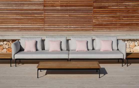 An outdoor sofa and a rectangular table by a stone and wood wall.