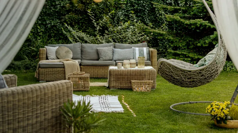 An outdoor relaxing area with a weaved sofa and tables, a chair surrounded by curtains.
