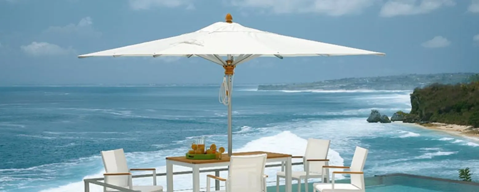 A dining table under a large umbrella by a beach.