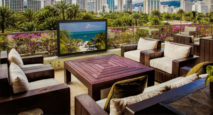 An outdoor TV in the middle of a sitting area under the sun.