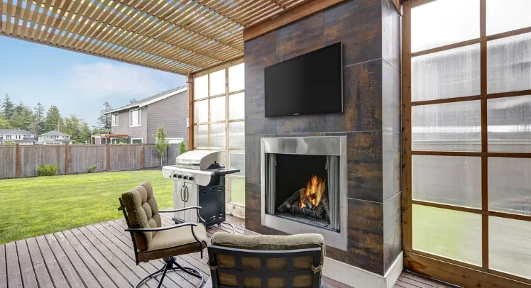 A TV on top of a fireplace in an outdoor sitting area.