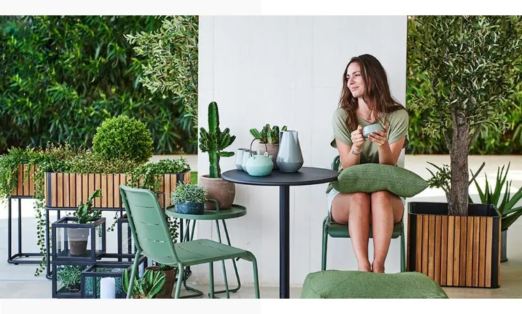 A woman sitting on a green chair by a small black round table holding a glass cup.