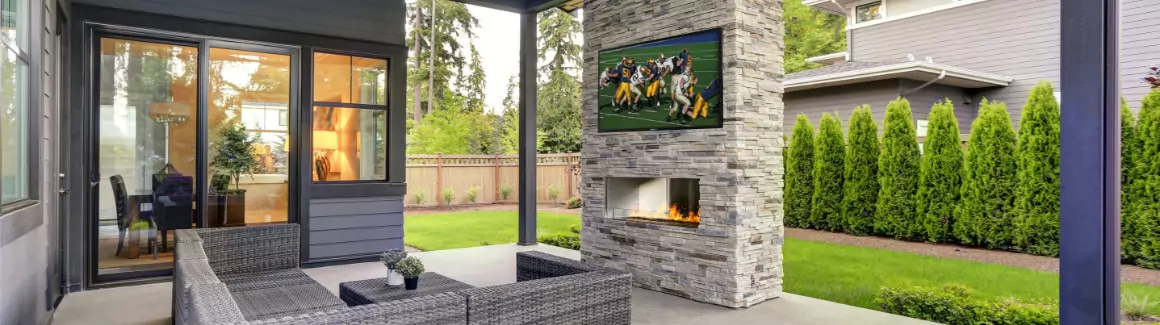 An outdoor sitting area with a fireplace and a TV hanging from the fireplace.