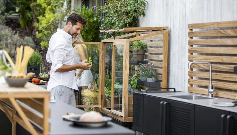 A man holding a plant in an outdoor kitchen.