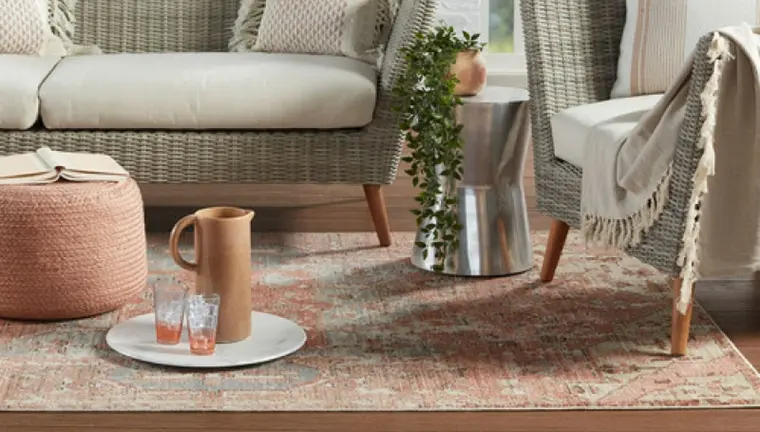 A wicker sofa and chair on a pink rug.