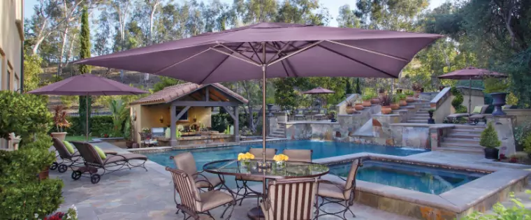 A dark brown umbrella covering a table by a pool.