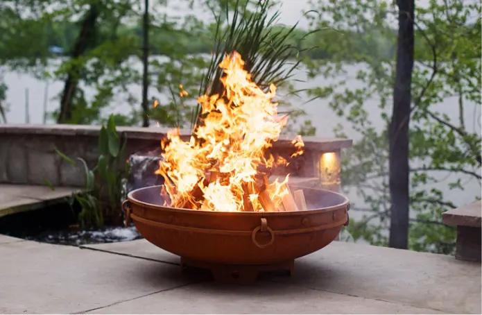 A round carbon steel fire bowl with burning wood.