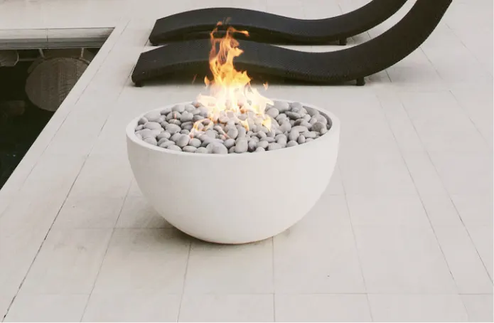 A white fire bowl on a wooden deck with burning fire rocks.
