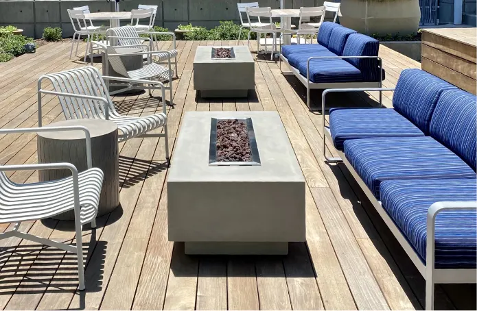 Two concrete fire tables side by side in front of blue sofas and metal chairs.