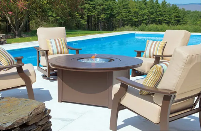 A brown plastic fire table surrounded by some chairs in front of a pool.