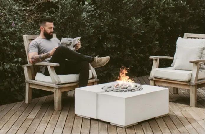 A man reading the newspaper in front of a square fire pit.