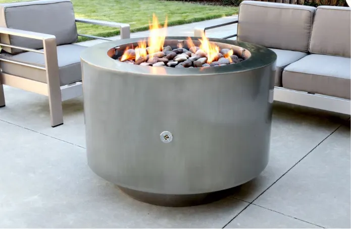 A round stainless steel fire pit in front of a sofa and chair.