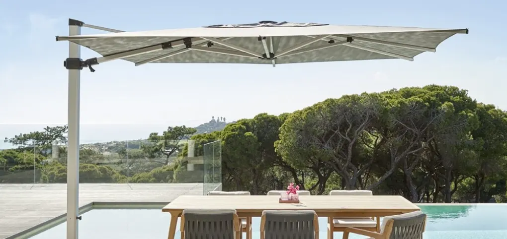A large umbrella over a dining table by a pool.