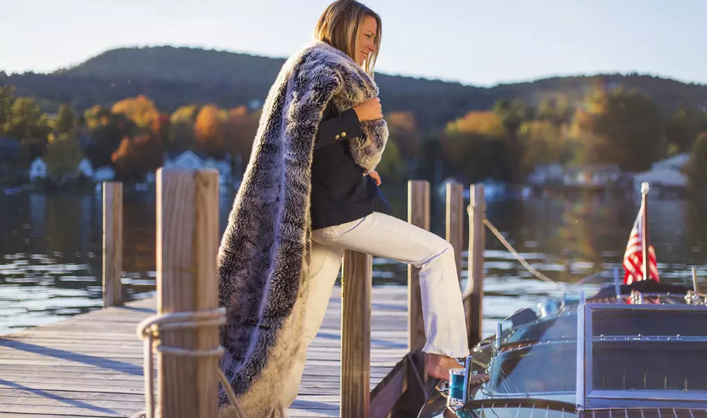 A woman stepping into a boat holding a faux fur coat.