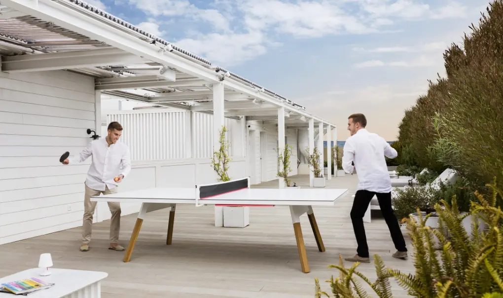 Two men wwith white shirts playing ping pong.