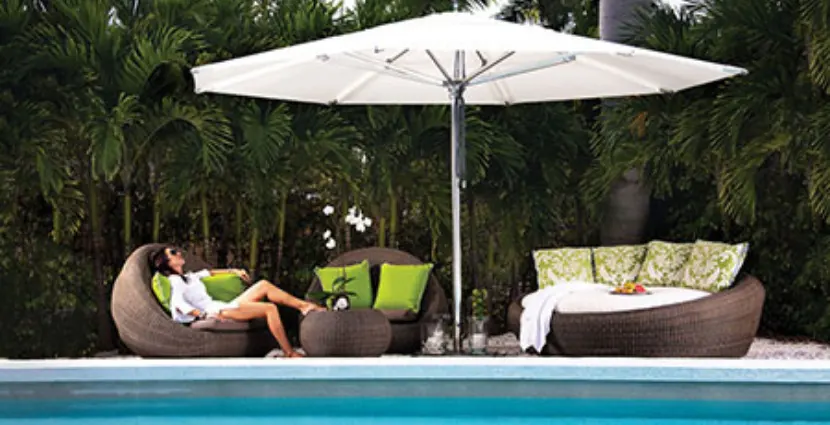 A woman sitting on a chair under a large white umbrella.