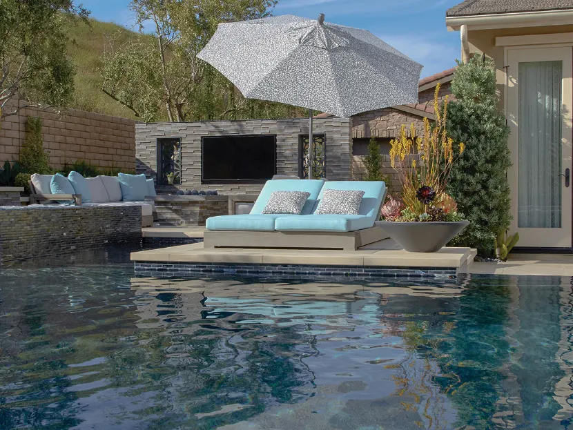 An umbrella with a black and white pattern over two chaise loungers in front of a pool.