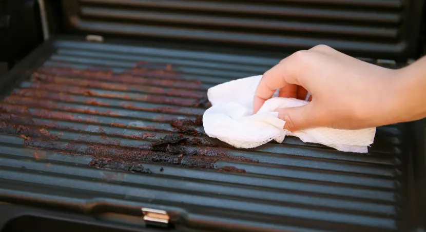 Someone cleaning a dirty grill with a wipe.