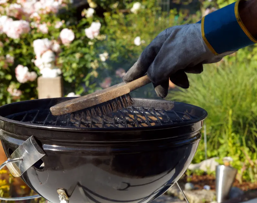 Someone with a heat-resistant glove cleaning a hot grill with a metal brush.