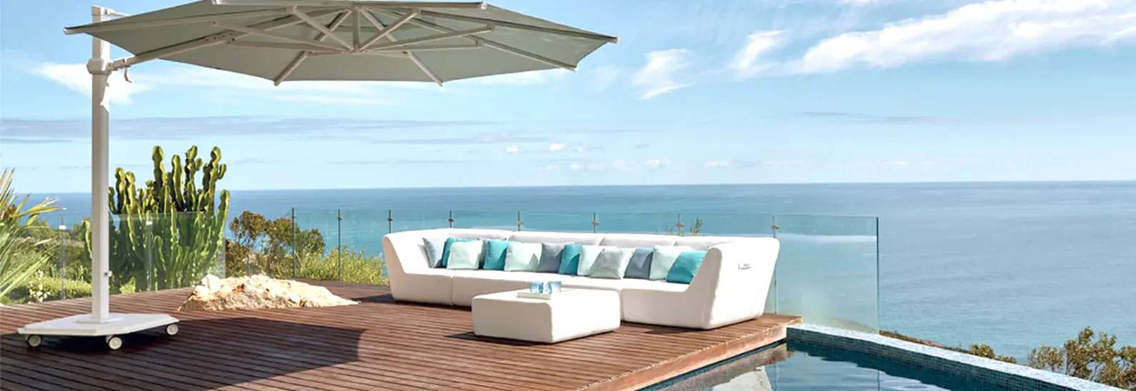 A deck with a glass fence with a white sofa next to a pool.