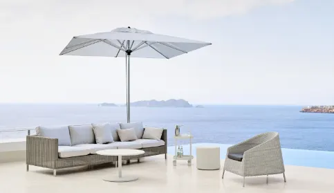 A sofa with a small round coffee table a side cart and chair with a large square umbrella covering them.