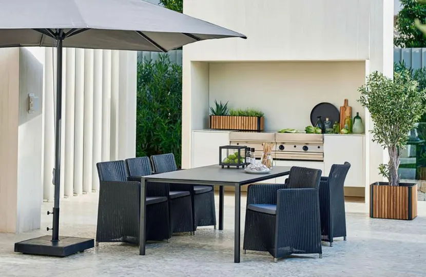 A large rectangular table with five woven chairs and a large umbrella.