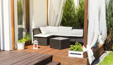 A pergola with a curtains attached to each post and a woven sofa inside.