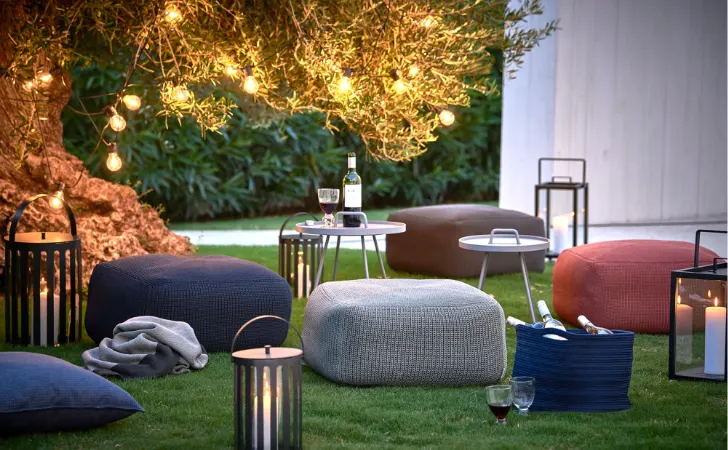 Various colored poufs and tables on the lawn by a tree with hanging lights.
