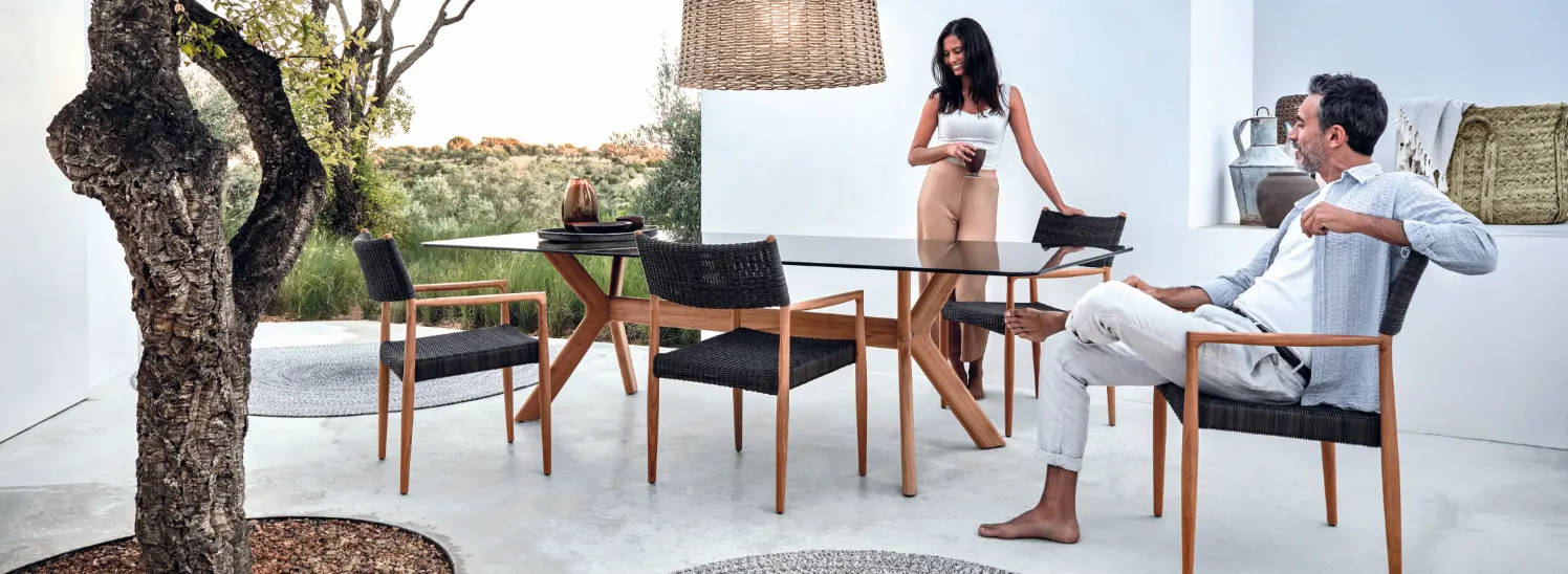 A woman standing behind an outdoor dining table while a man sits in front of it.