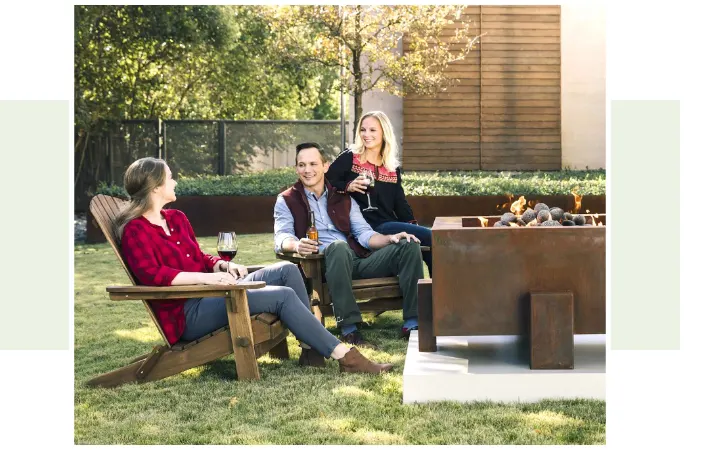 Two women and a man sitting by a fire pit having a conversation.