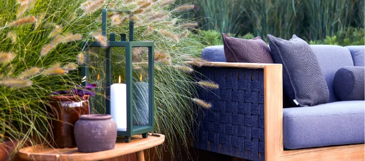 A blue sofa next to a plant and a table that has a lantern and some vases on it.