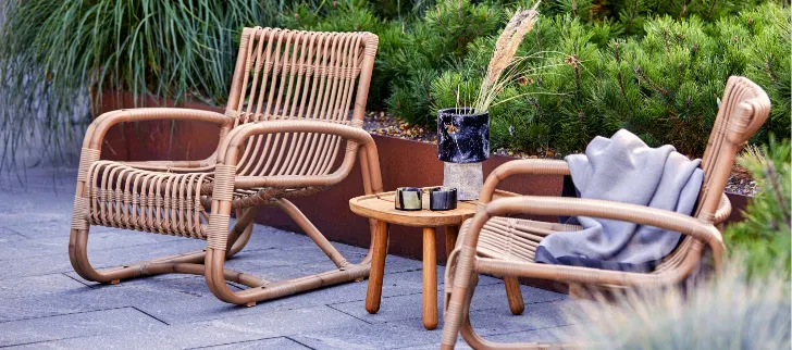 Two teak chairs with a small accent table in between them.