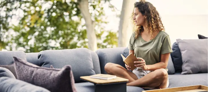 A woman sitting on a sectional reading a book.