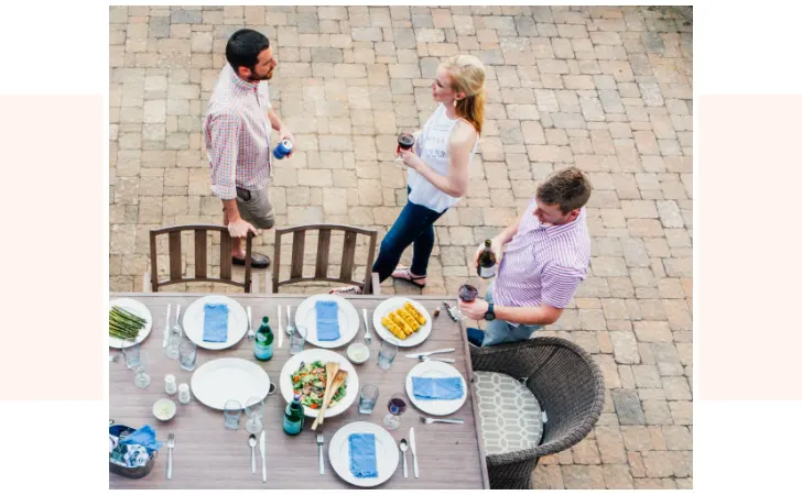 A couple talking by a dining table while another man is pouring a glass of wine.