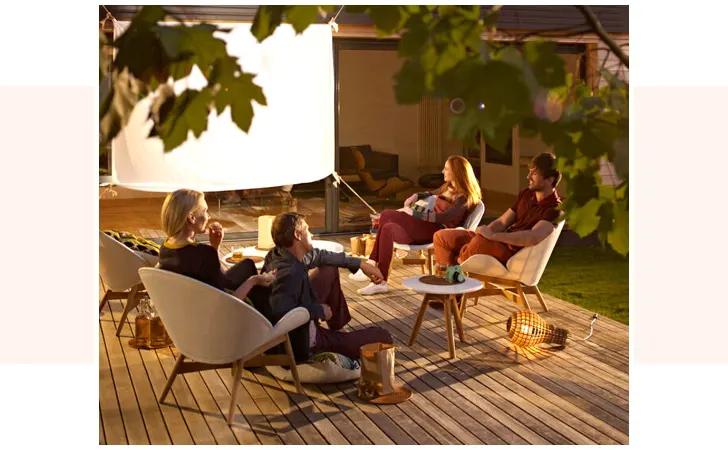 Two couples sitting on a deck by a large white projector screen.