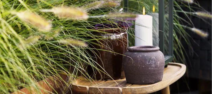 A table with some vaseds and a lit candle by some plants.