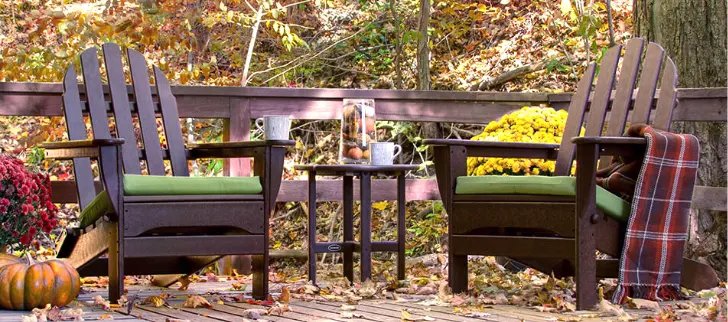 Two chairs on a deck with a small round table in between them.