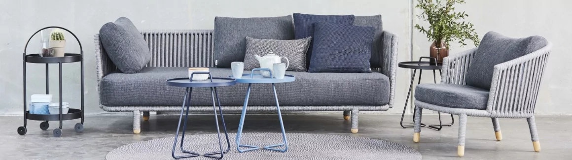 A gray sofa with a wicker accent chair and two small tables in front.