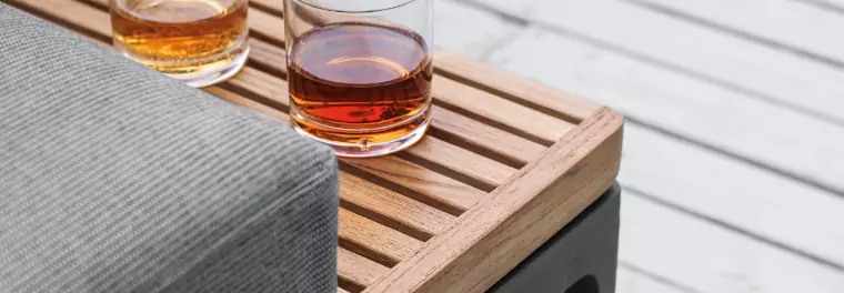 Two glasses with liquor on top of a teak table.