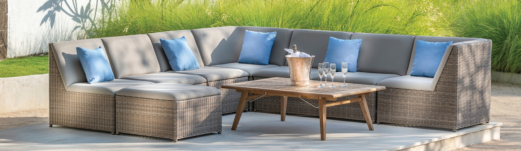 A gray outdoor sectional with a center table filled with ice and a champagne bottle and four glasses on the table