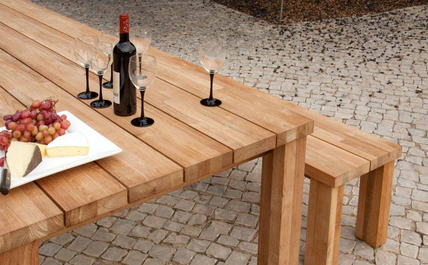 Wine bottle, wine glasses, cheese, and grapes on a Table with a bench