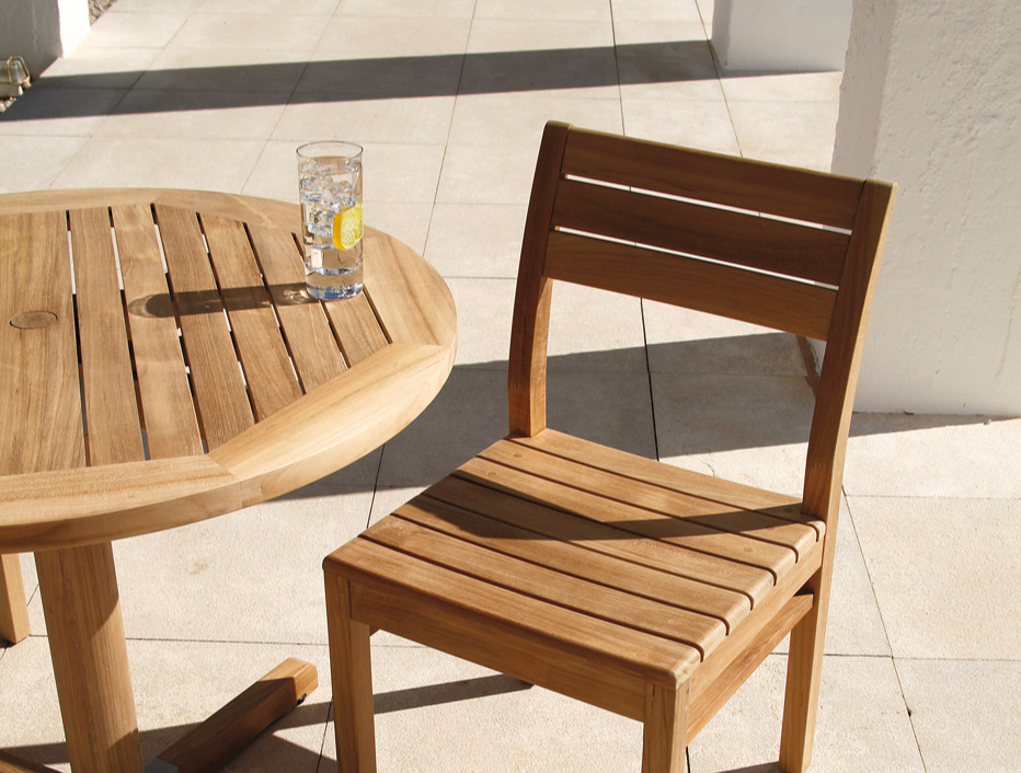 A glass of water on a Teak Table with a chair on front