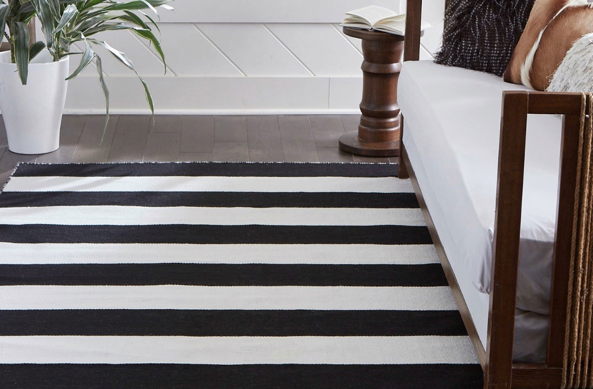 A black and white rug in front of a teak sofa.
