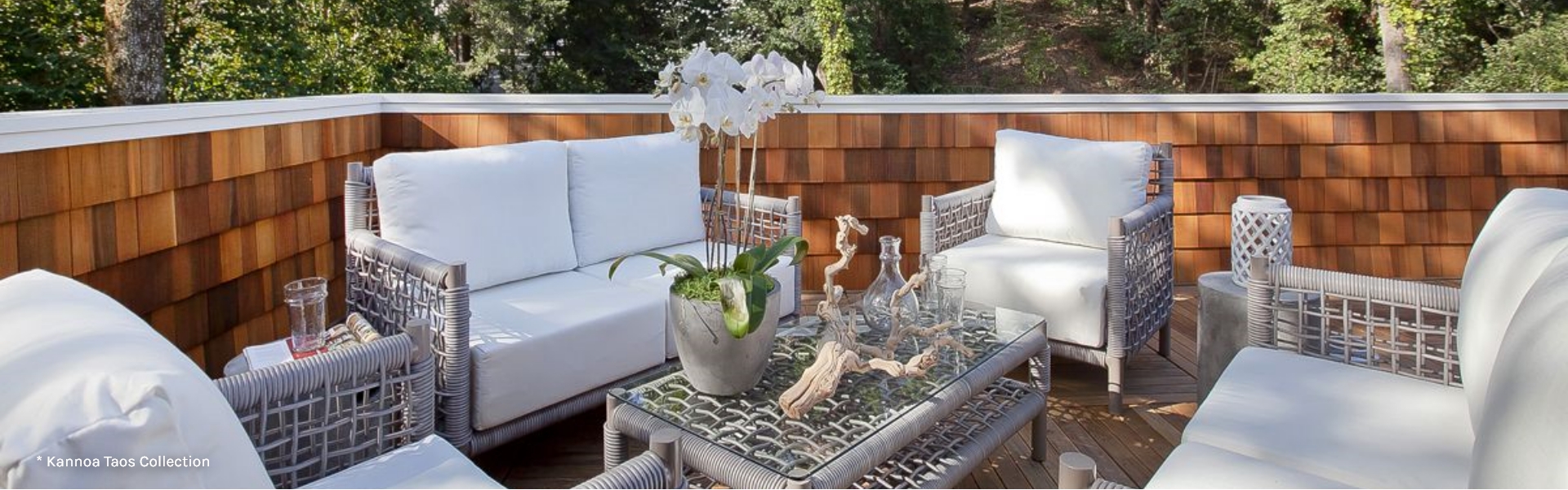 Outdoor sitting area with two sofas and two chairs with white cushions and a center table with a planter with white flower